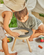 Close up of two children crouched around the PlanToys BBQ toy, lifting up the grate to look inside