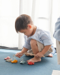 Young child crouched down playing with the PlanToys wooden fishing game set on a blue carpet