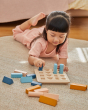 Girl laying down on a carpet placing shapes into the PlanToys plastic-free wooden shape sorter
