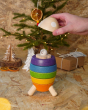 Close up of hand holding a piece of the PlanToys wooden stacking rocket toy above the astronaut, in front of a small Christmas tree