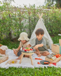 Two children sat on a blanket in front of a small tent playing with wooden play food on top of the PlanToys wooden BBQ set