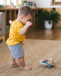 Child walking backwards on a beige carpet pulling the PlanToys wooden musical xylophone bear toy