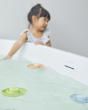 Close up of 3 PlanToys natural rubber bath toys floating in some water in front of a young girl