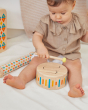 Close up of young child playing with the PlanToys solid wooden drum toy on a white blanket