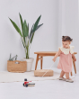 Girl pulling the PlanToys wooden musical drummer toy along a white floor next to a wooden table and potted plant