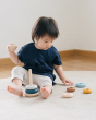 Child sat on a grey carpet playing with the PlanToys plastic-free wooden stacking orchard rings