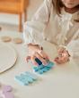 Young girl lining up blue pieces from the PlanToys Waldorf mandala set on a white table