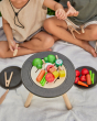 Close up of two children playing with some play food vegetables on top of the PlanToys BBQ role play set