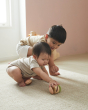 Two young children crawling on the floor reaching for the PlanToys clapping roller sensory toy