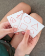 Close up of children's hands holding the prompt drawing cards from the PlanToys wooden touch and guess feeling game