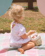 A child sitting with their back towards the camera holding the Olli Ella Rattan Berry Basket with Lining – Pansy Floral. A beautifully woven rattan basket with cream cotton lining with a vintage pansy floral pattern.