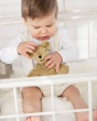 A child playing contently whilst sat in a white cot, with the Senger baby animal bear toy.
