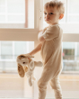 A child stood by a window and wearing a beige outfit whilst holding the Senger Cuddly Animal Organic Soft Toy - Small Dog
