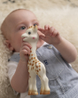 A child laid down on a fluffy rug, grasping the Sophie la Girafe® - Once Upon A Time 100% Natural Rubber Original Giraffe Teether