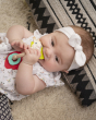 A child laid down on a multi-coloured rug, chewing on the Sophie The Giraffe - Nature Chew Rattle