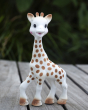 A closer view of the Sophie la Girafe® - Once Upon A Time 100% Natural Rubber Original Giraffe Teether, showing the brown hoofs and spots, rosy cheeks and brown tipped ears and ossicones, with a large leafy green plant in the background