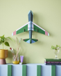 Studio Roof plastic-free card aeroplane on a green wall above a potted plant and some books