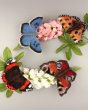 The Makerss Needle Felt Butterflies including the Peacock, Blue, Tortoiseshell and Admiral butterflies sat or an arrangement of pink and white flowers