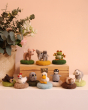 The Makerss - Amiguwoolli Tiny Mini Needle Felt Figures. 10 mini needle felt figures lined in two rows. Sat on top of a wooden box is the mini pig, elephant and frog, and on the bottom is the snoozing bear, chicken, tiny owl, duck, tiny penguin, guinea pi