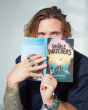 Author Dougie Poynter holding The Whale Watchers childrens book up in front of his face on a grey background