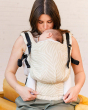 Woman wearing a Tula FTG baby carrier in the savannah print, looking down and kissing the head of a baby sleeping inside the carrier
