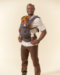 Man stood on a beige background with a baby inside a Tula explore baby carrier