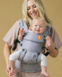 Woman stood wearing a front facing Tula explore baby carrier in the rain colour on a beige background