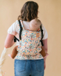 Close up of woman stood backwards with a baby on her back in a Tula free to grow charmed carrier