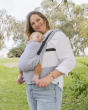 Woman stood in a park with a baby in a Tula free to grow baby carrier