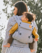 Close up of woman walking under some trees carrying a baby in the Tula explore rain baby carrier