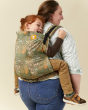 Woman stood backwards on a beige background, carrying a child in the Tula preschool meadow carrier