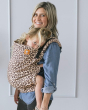 Woman stood in front of a grey wall carrying a little girl in a Tula soft pre-school leopard print carrier