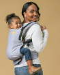 Close up of woman carrying young girl on her back in the Tula free to grow baby carrier in the rain blue colour