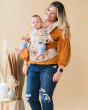 Woman stood on a beige background with a forward facing Tula explore baby carrier in the charmed print