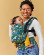 Woman stood on a yellow background with a baby in a Tula free to grow baby wearing carrier