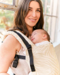 Close up of a woman wearing a Tula free to grow carrier with beige zebra stripes, and a sleeping baby inside