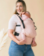 Woman carrying a baby in a Tula stardust FTG baby carrier on a beige background
