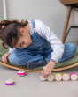 A child sitting on a Wobbel board, playing with Wobbel Cookies and the Wobbel Big Macaron, on a grey coloured floor