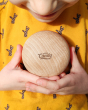 A child in an orange t-shirt holding the Wobbel Candy Big Macaron in their hand. The Big Macaron shows the natural Beech wood texture and wood grain