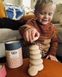 A child almost finishing a Wobbel Wooden Candy Drops Stack, in Marrakesh on a Wobbel Board. The cardboard tube tin is stood next to the stack