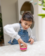 A child playing and spinning a Wooden Wobbel Candy Big Macaron on a  table. Made from Beech wood with a pink "filling", perfect for games, rolling, sliding, wobbling, spinning