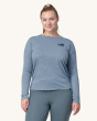 An adult wearing a Patagonia Women's Long-Sleeved Capilene Cool Daily Graphic Shirt, showing the fit of the top from the front and wearing light grey leggings