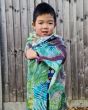 Young boy wrapped up in a large wonder cloth in front of a wooden fence