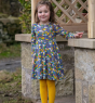 a girl wearing blue organic cotton dress with a rainbow weather and planets all-over print, long sleeves, and a twirly circle skirt from piccalilly