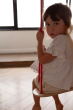 Close up of child sat on a Babai eco-friendly wooden rope swing in a bright living room