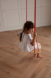 Child swinging on a Babai sustainable wooden rope swing above a wooden floor