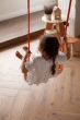 Child swinging on a terra Babai sustainable rope swing above a wooden floor next to a set of Babai stools and table