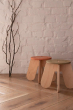 Khaki and terra babai sustainable wooden stools on a wooden floor in front of a white brick background