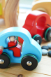 Eco-friendly Bajo fasten seatbelts car on a wooden background in front of a wooden tree toy and a red bajo fasten seatbelts car