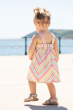 Child wearing the Frugi Stripe dress Beach Party Dress showing the back of the dress, the sea can be seen on the background 